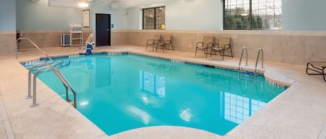 An indoor swimming pool with clear water, a lifeguard chair, and a window with a view.