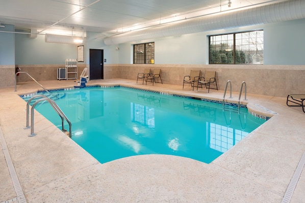 Una piscina interior con agua cristalina, una silla de salvavidas y una ventana con vistas.