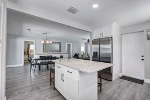 A modern kitchen with a marble island, stainless steel appliances, and a dining area with a chandelier. - E. Boca Heated Pool Home/1 Mile to Beach + Mizner (Boca Raton)
