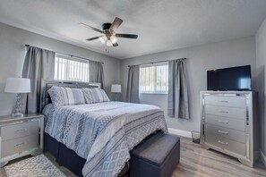 Ein Schlafzimmer mit einem Bett, Nachttischen, einer Kommode, einem Fernseher und einem Deckenventilator.