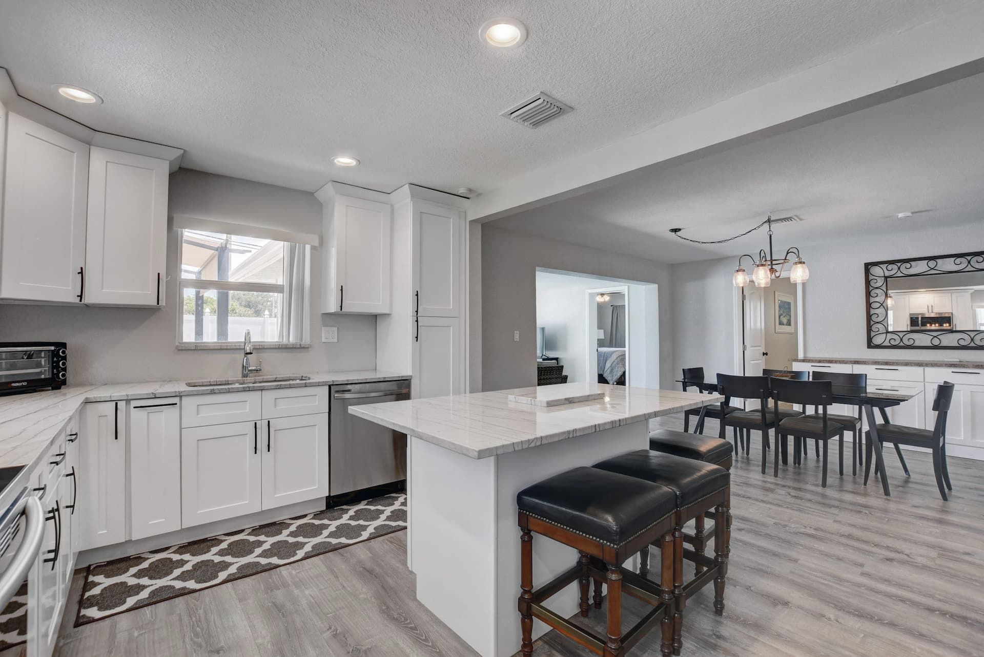 A modern kitchen with white cabinetry, a marble countertop, and a central island with bar stools.