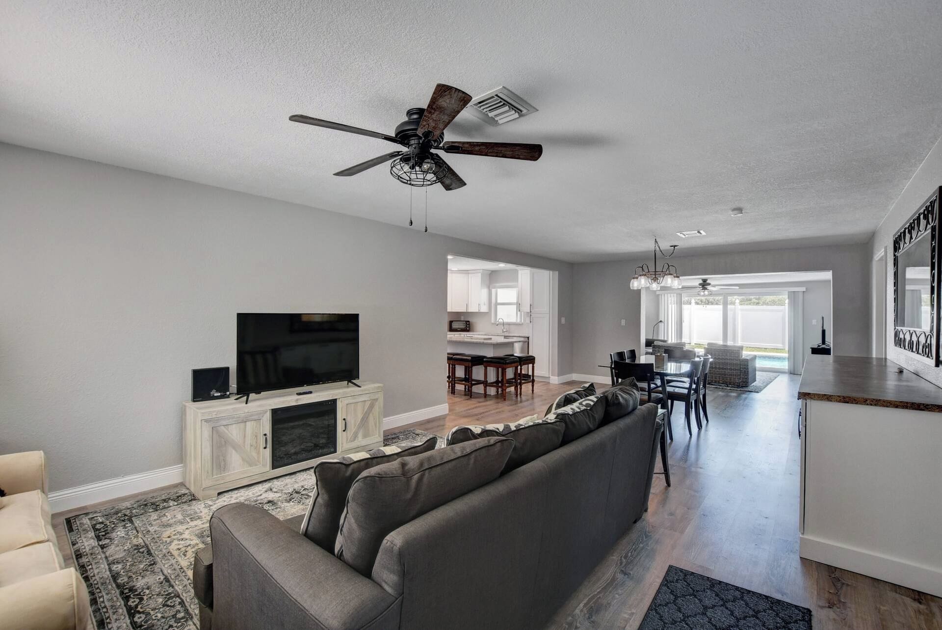 A modern living room with a flat-screen TV, a grey sofa, and a ceiling fan.