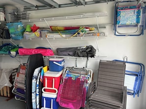 A storage area with shelves holding various items like bags, containers, and a blue chair. - E. Boca Heated Pool Home/1 Mile to Beach + Mizner (Boca Raton)