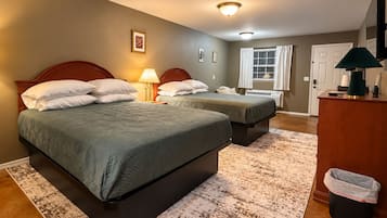 A hotel room with two beds, a desk, a trash bin, and a window with curtains.