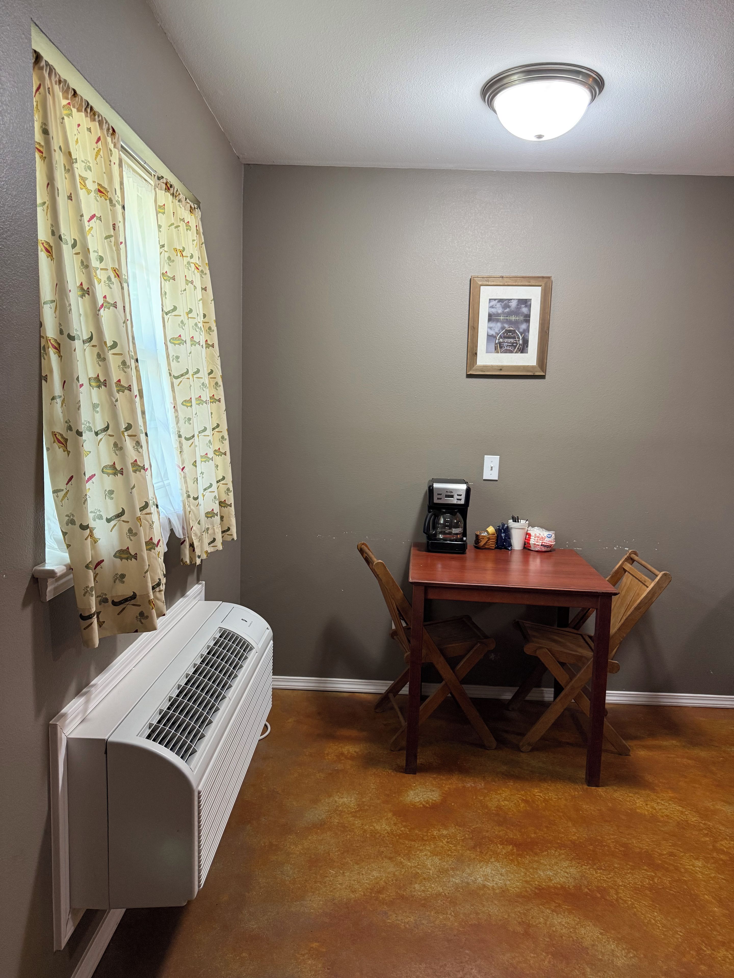 A dining area with a table, chairs, a coffee maker, and a wall-mounted picture.