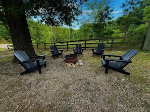 An outdoor seating area with Adirondack chairs arranged around a fire pit. - The Grove  2 — Rustic River Lodge Room (TAHLEQUAH)