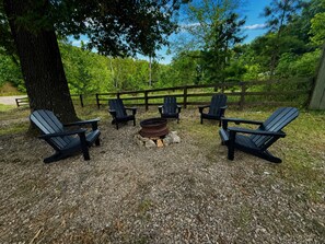 An outdoor seating area with Adirondack chairs arranged around a fire pit. - The Grove 3 — Rustic River Lodge Room (TAHLEQUAH)