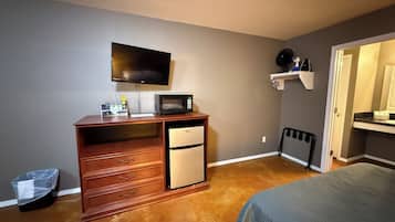 A compact hotel room with a bed, a desk with a microwave, a small refrigerator, and a television on the wall.