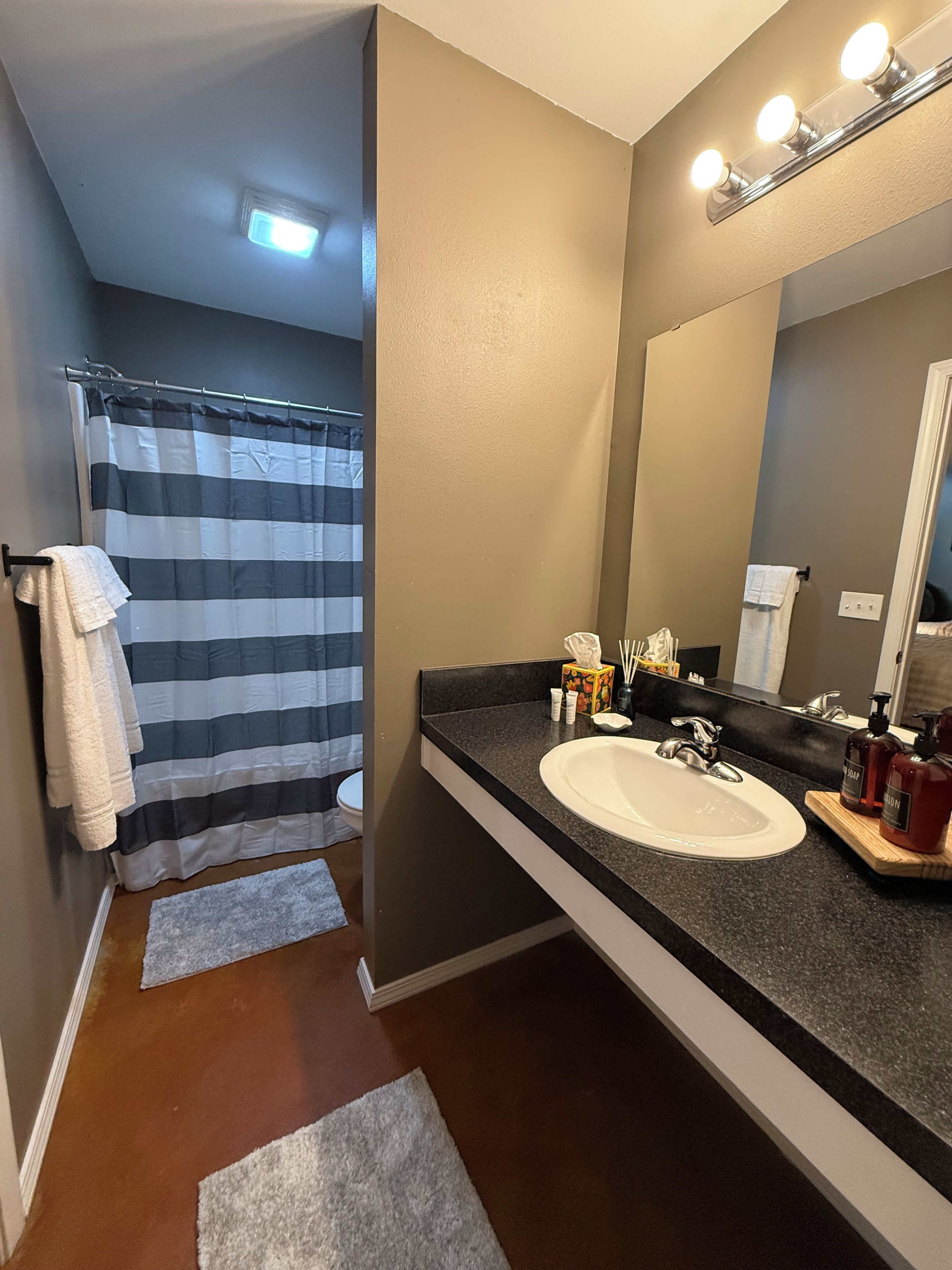 A bathroom with a striped shower curtain, a white sink, a mirror, and toiletries.