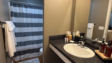A bathroom with a striped shower curtain, a white sink, a mirror, and toiletries.