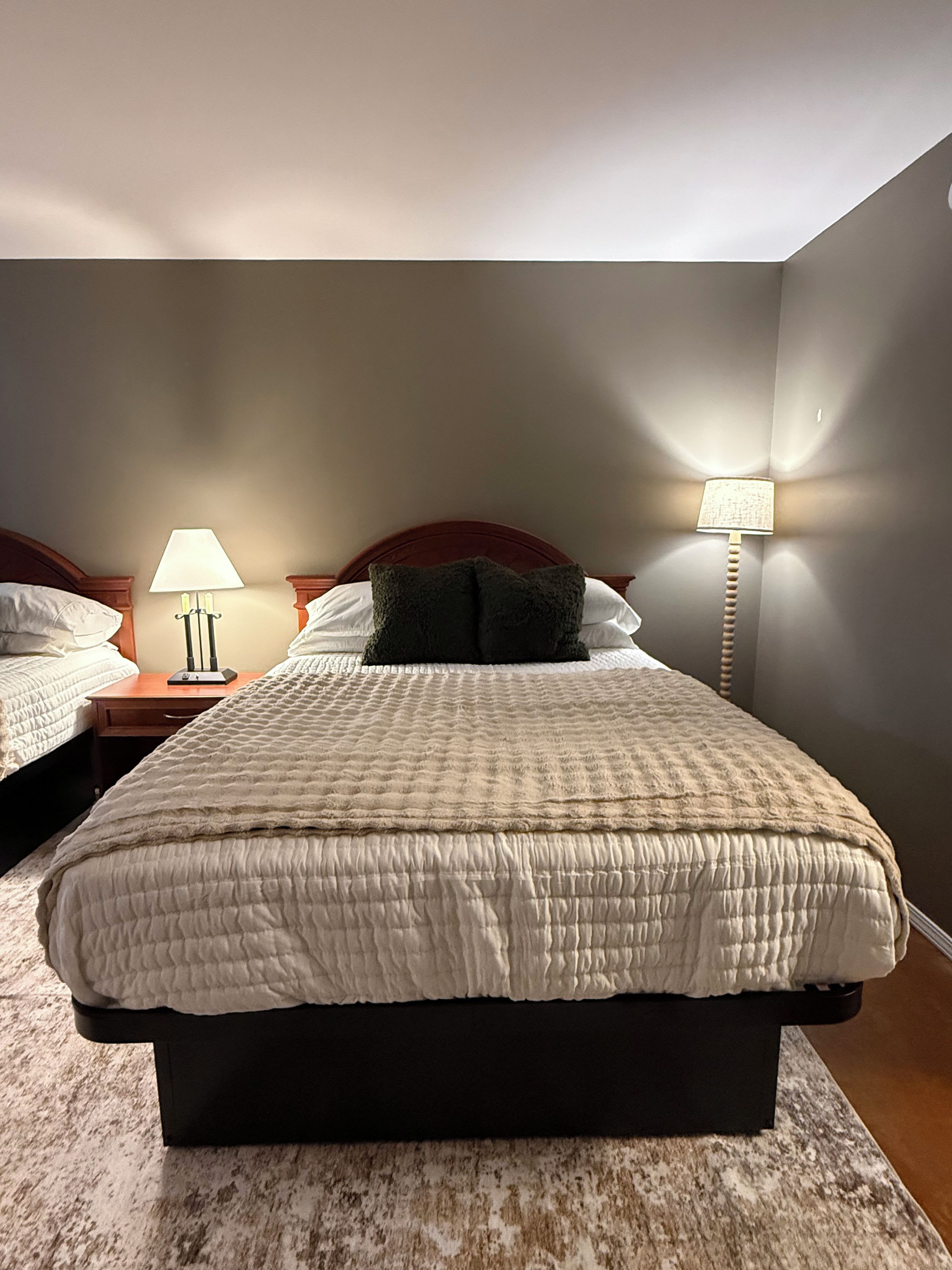 A bedroom with a large bed, two bedside tables, a lamp, and a wall-mounted light fixture.