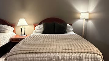 A bedroom with a large bed, two bedside tables, a lamp, and a wall-mounted light fixture.
