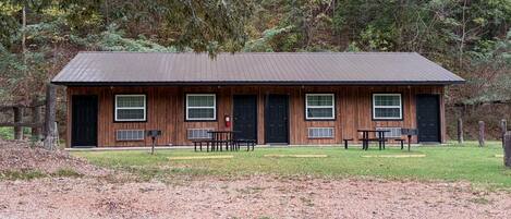 A rustic cabin with a gravel driveway, wooden benches, and a metal roof.