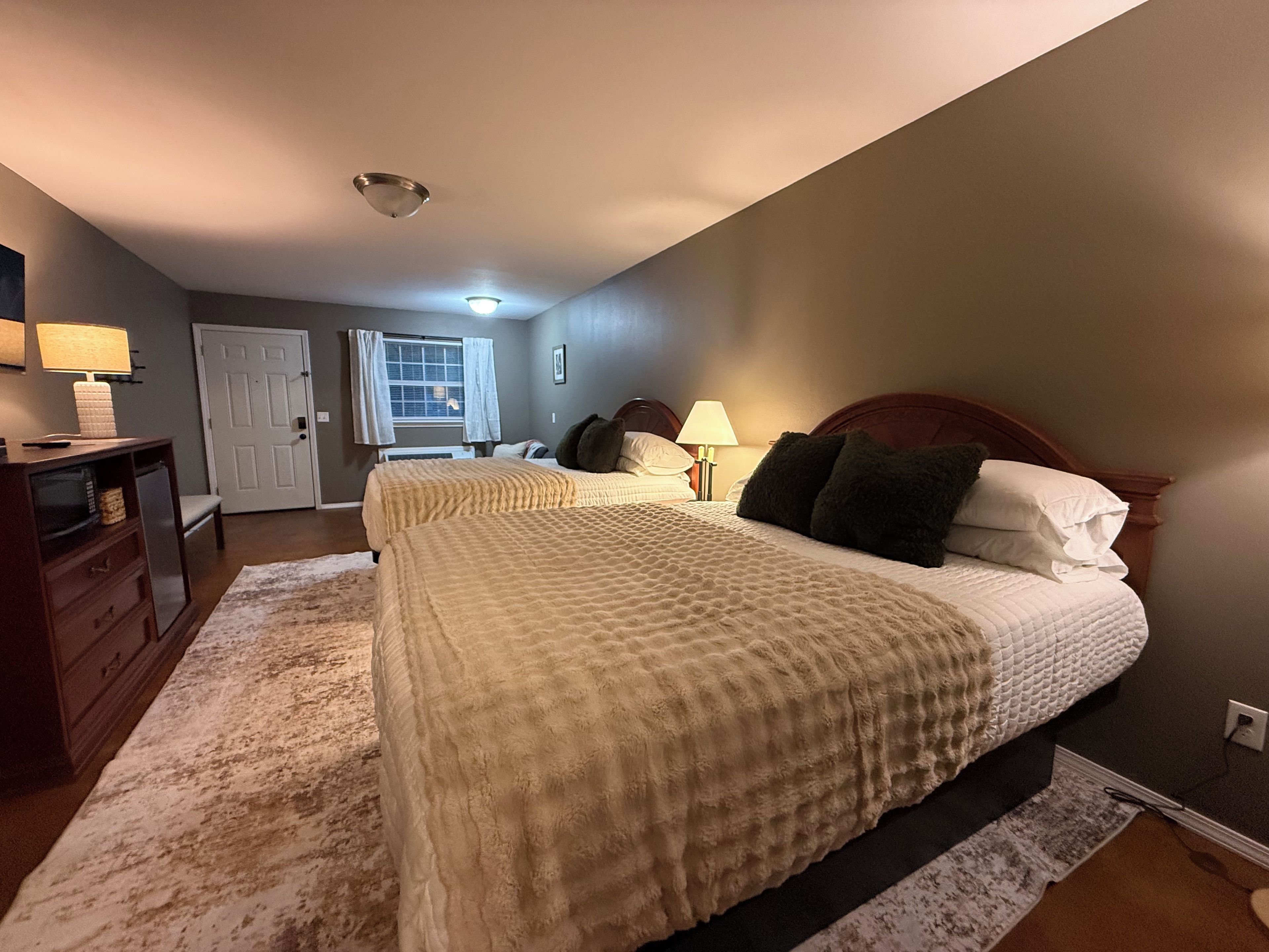 A bedroom with a large bed, bedside lamps, a dresser, and a door leading to another room.