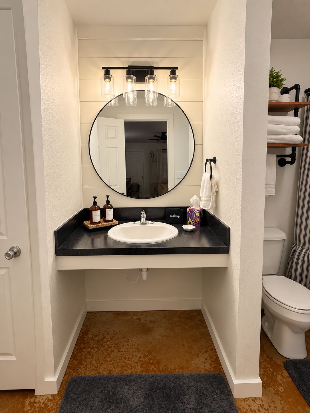 A bathroom with a white vanity, a round mirror, a sink, and a toilet.