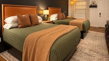 A hotel room with two beds, a ceiling fan, a bedside lamp, a patterned rug, and a door.