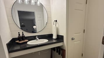 Une salle de bain avec un lavabo blanc, un miroir rond et un porte-serviettes.