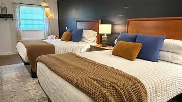 A hotel room with two beds, a ceiling fan, a nightstand with a lamp, and a window with blinds.