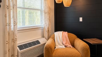 A room with a window, air conditioning unit, a brown sofa with a blanket, and a wooden table.