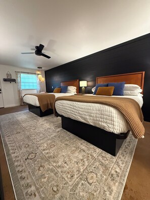 Un dormitorio con dos camas, ventilador de techo, lámparas de noche y una alfombra estampada.