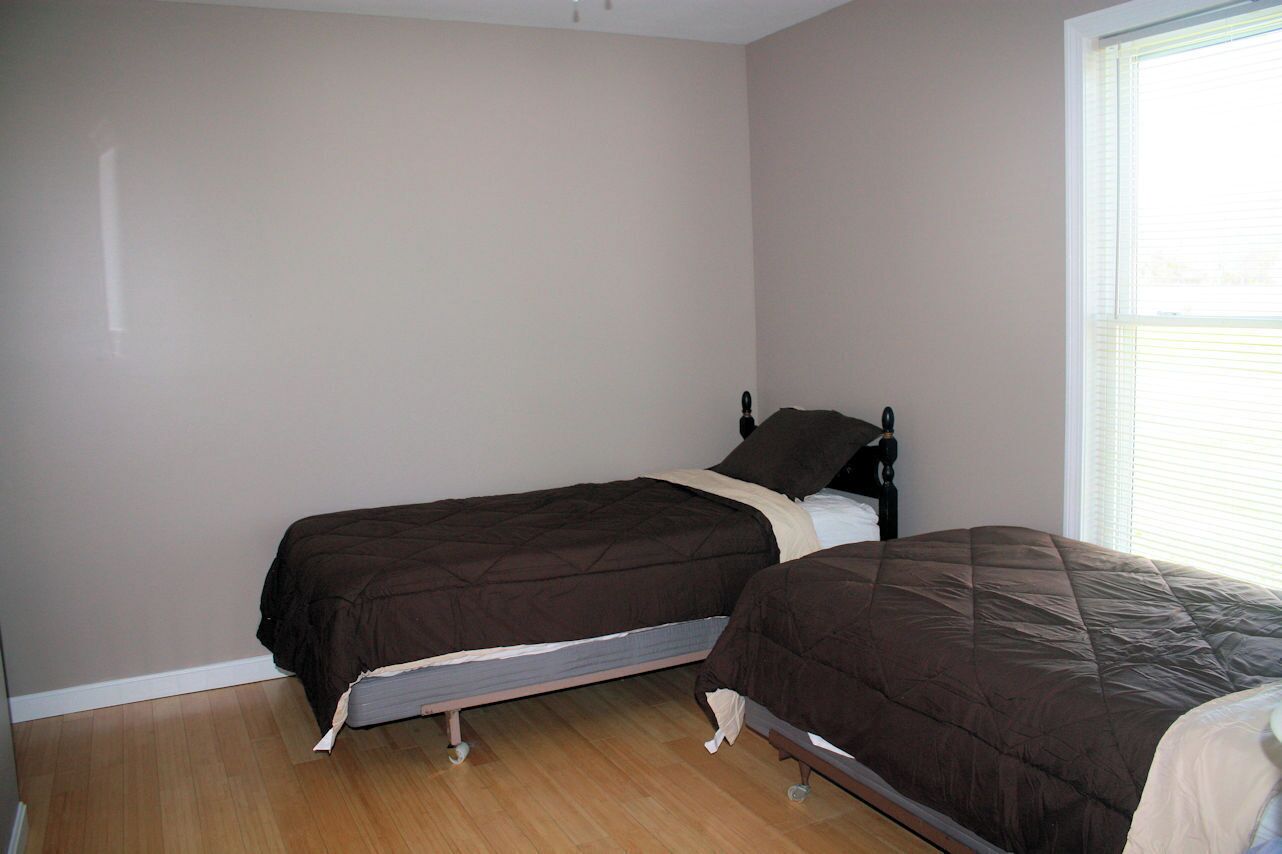 Une chambre avec deux lits simples, une fenêtre avec des stores et un plancher en bois.