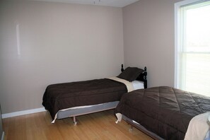 A bedroom with two single beds, a window with blinds, and a wooden floor.