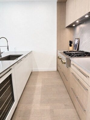 A modern kitchen with white cabinetry, a stainless steel sink, and a gas stove. - Mira | Lakeside Serenity • Pool, Sauna & Gym (Kelowna)