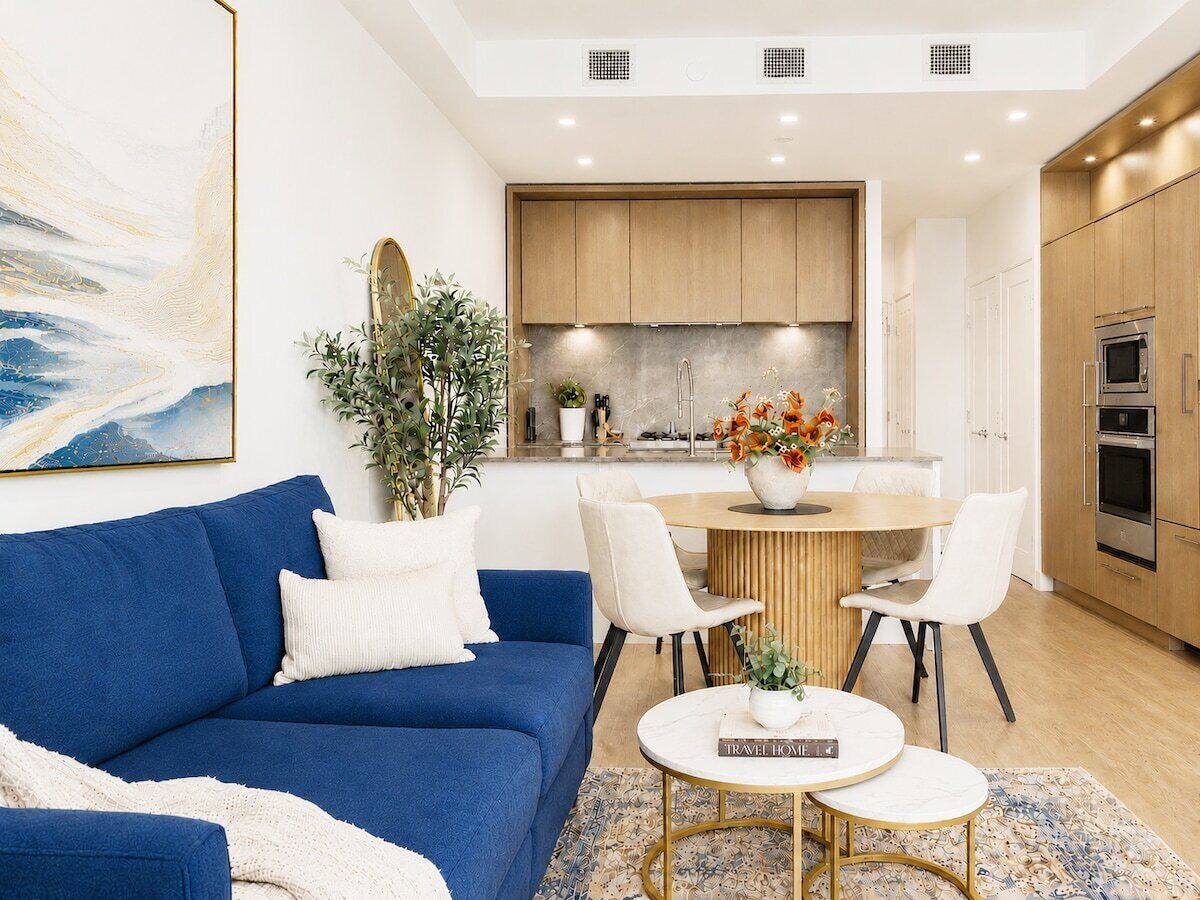Un salon moderne avec un canapé bleu, un coin repas avec une table blanche et une cuisine dotée de meubles en bois.