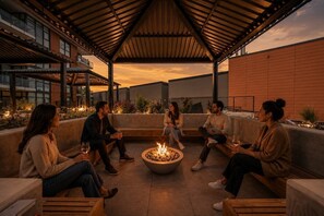 Eine Gruppe von Personen sitzt um eine Feuerstelle auf einer überdachten Terrasse mit moderner Architektur.