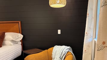 Un dormitorio con cama, una mesita, una silla, un calefactor y una lámpara fijada a la pared.