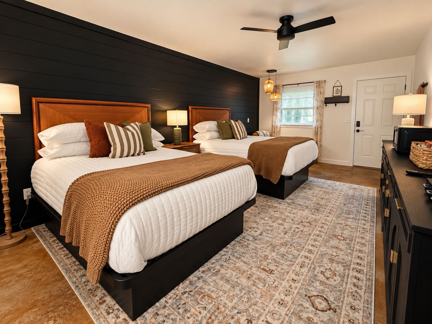 A bedroom with two beds, a ceiling fan, bedside lamps, a patterned rug, and a dresser with a lamp.