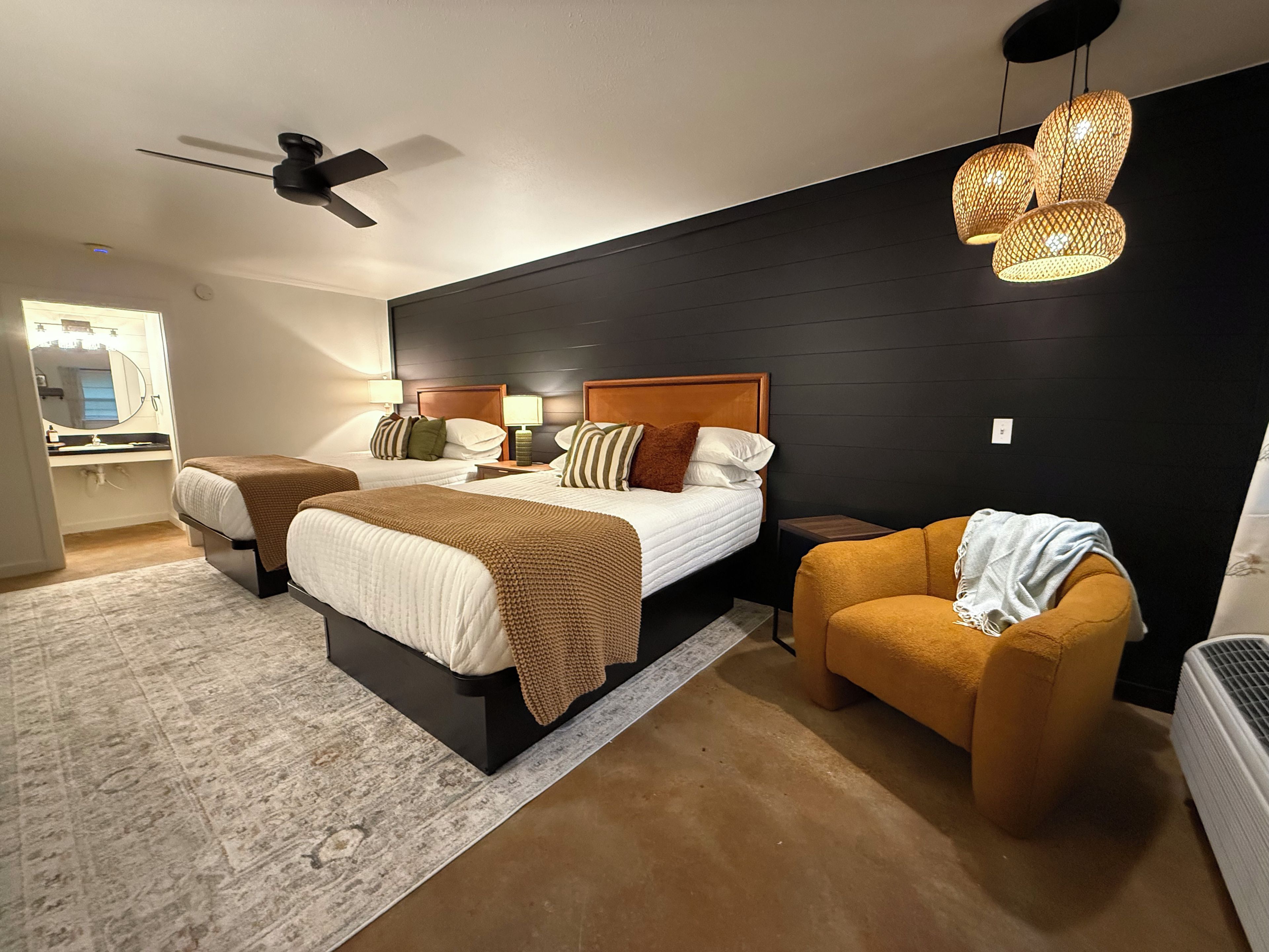 A hotel room with two beds, a sitting area, a ceiling fan, and a modern light fixture.