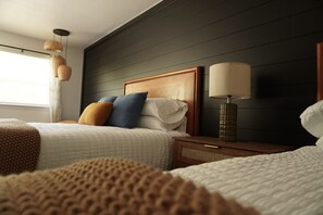 Habitación de hotel con dos camas, una mesita de noche con lámpara y una ventana con cortinas.