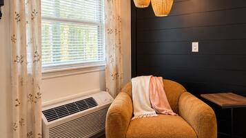 A room with a window, air conditioning unit, a brown sofa with a blanket, and a wooden table.