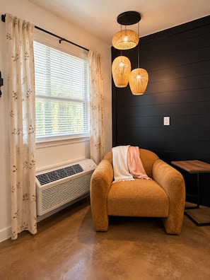 Una habitación con ventana, unidad de aire acondicionado, un sofá marrón con una manta y una mesa de madera.