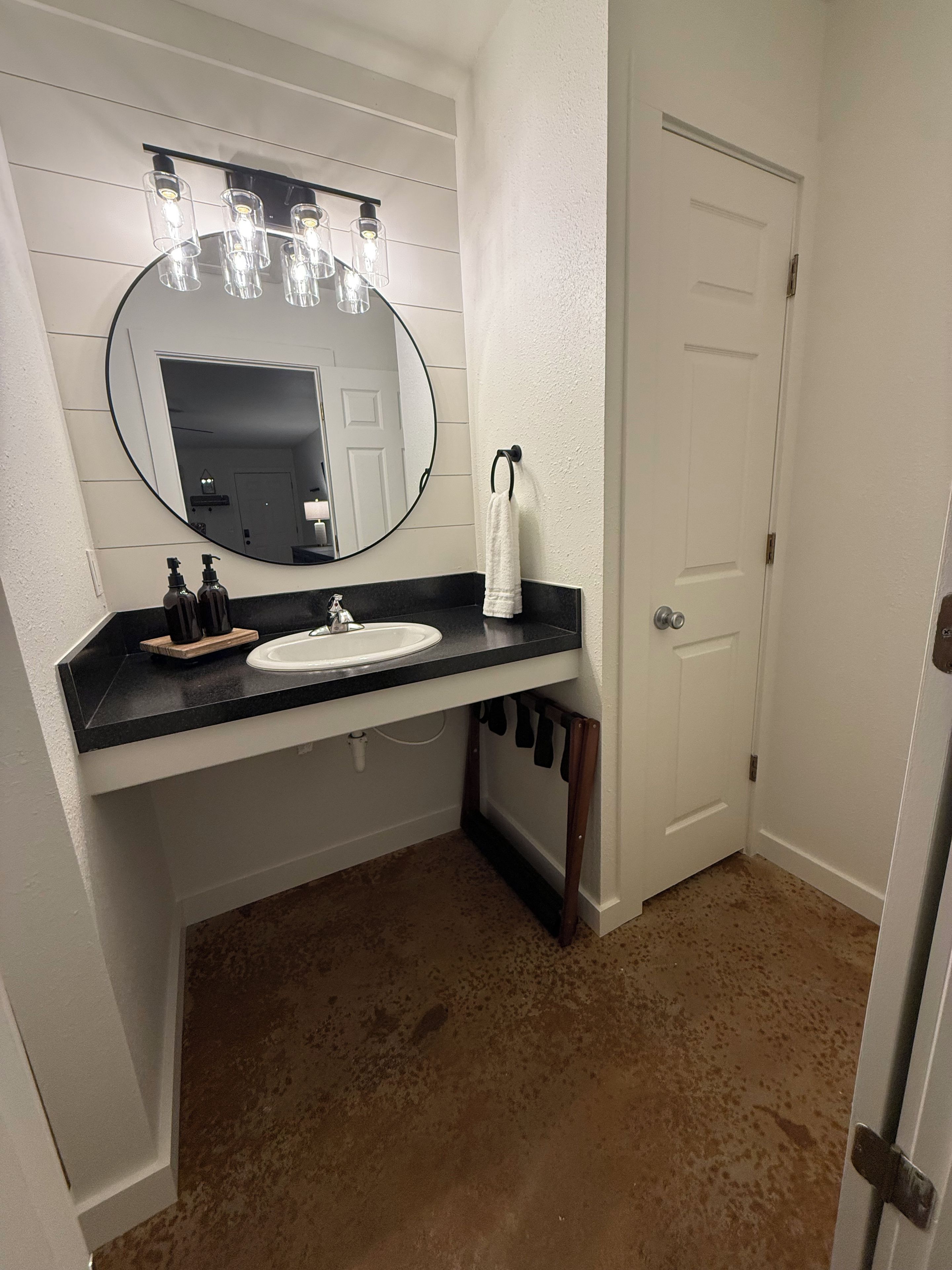 A bathroom with a white sink, a round mirror, and a towel rack.
