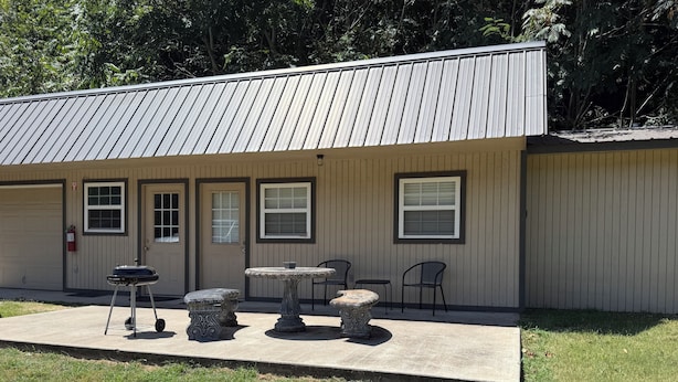 A building with a garage door, a small patio with a table and chairs, and a fire hydrant. - Welcome to The Eddy, our family-friendly room at The Lodge on Ten (TAHLEQUAH)