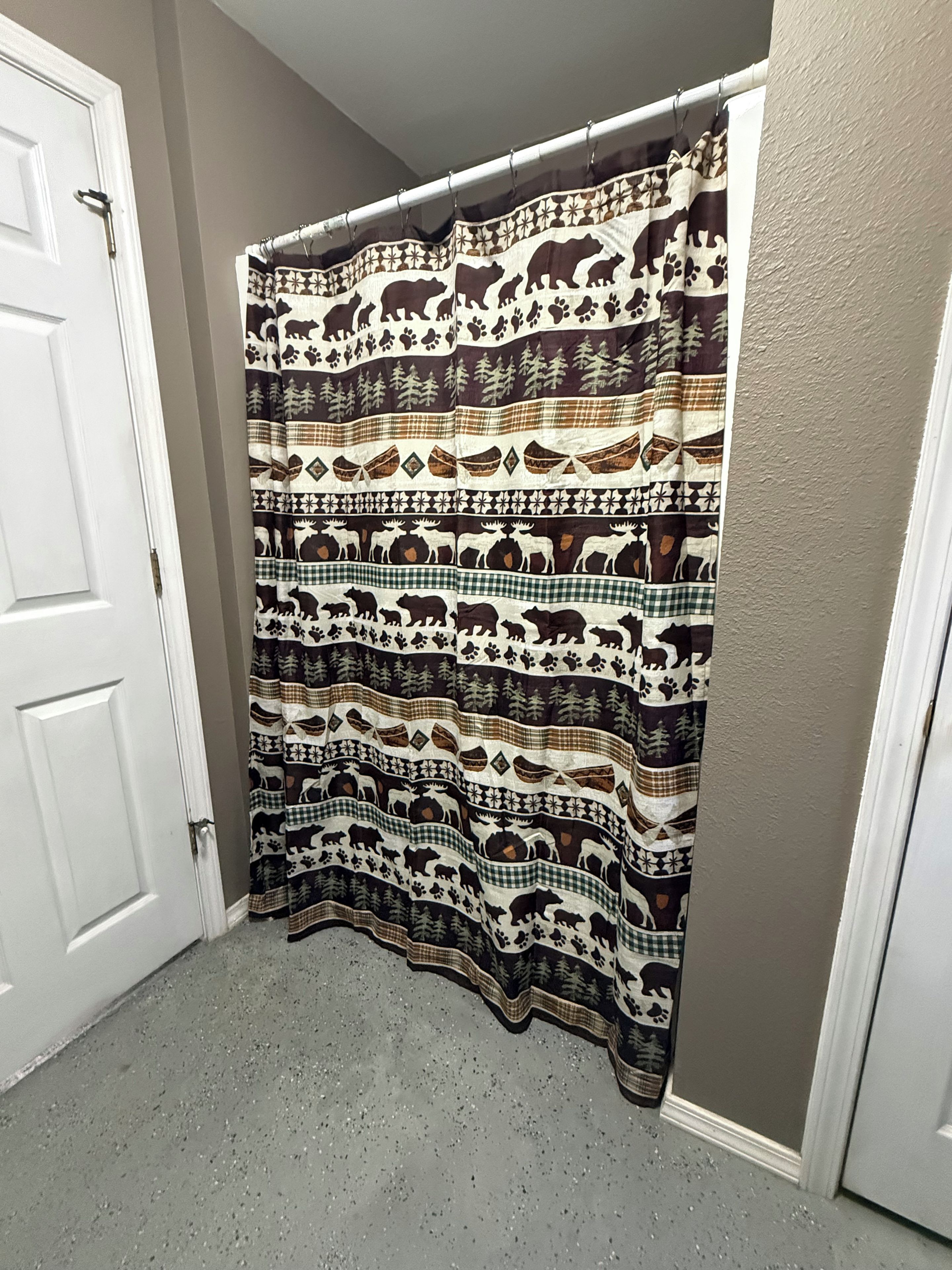 Un baño con cortina de ducha estampada con motivos de animales, una puerta blanca y un suelo moteado.