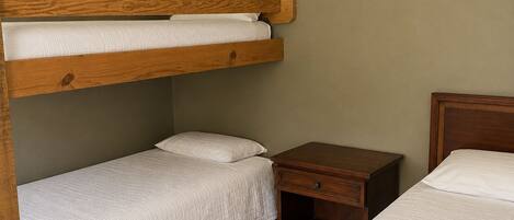 Une chambre avec un lit superposé doté d’une tête de lit en bois, d’une table de chevet et d’une petite table de nuit.
