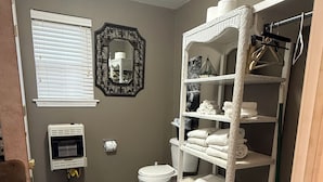 A bathroom with a toilet, a white laundry basket, and a white shelf unit with towels. - Welcome to The Eddy, our family-friendly room at The Lodge on Ten (TAHLEQUAH)