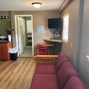 A compact living space with a kitchenette, a sofa, a dining table, and a television mounted on the wall. - Welcome to The Eddy, our family-friendly room at The Lodge on Ten (TAHLEQUAH)