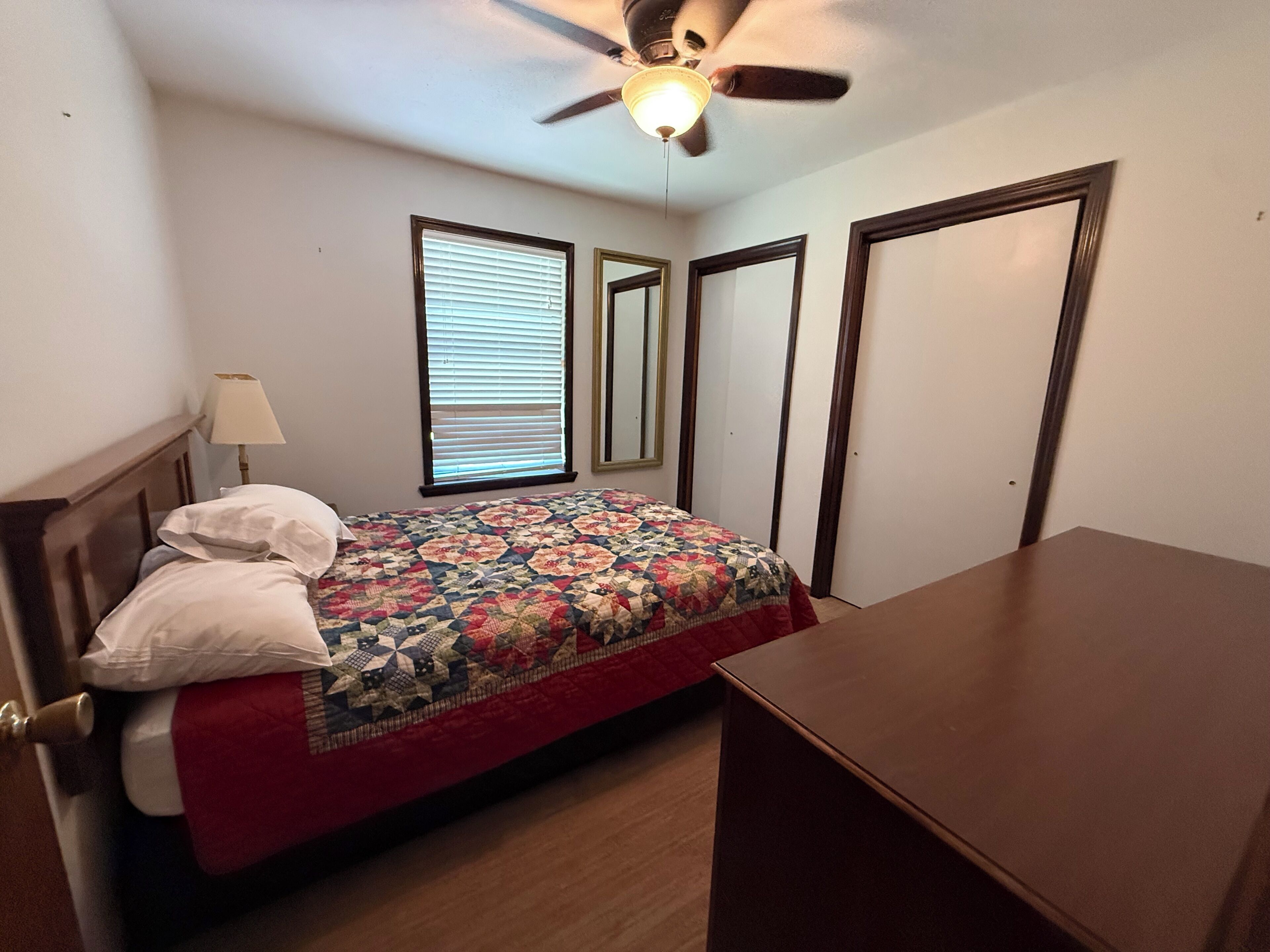 A bedroom with a bed, a ceiling fan, a window with blinds, and a door.