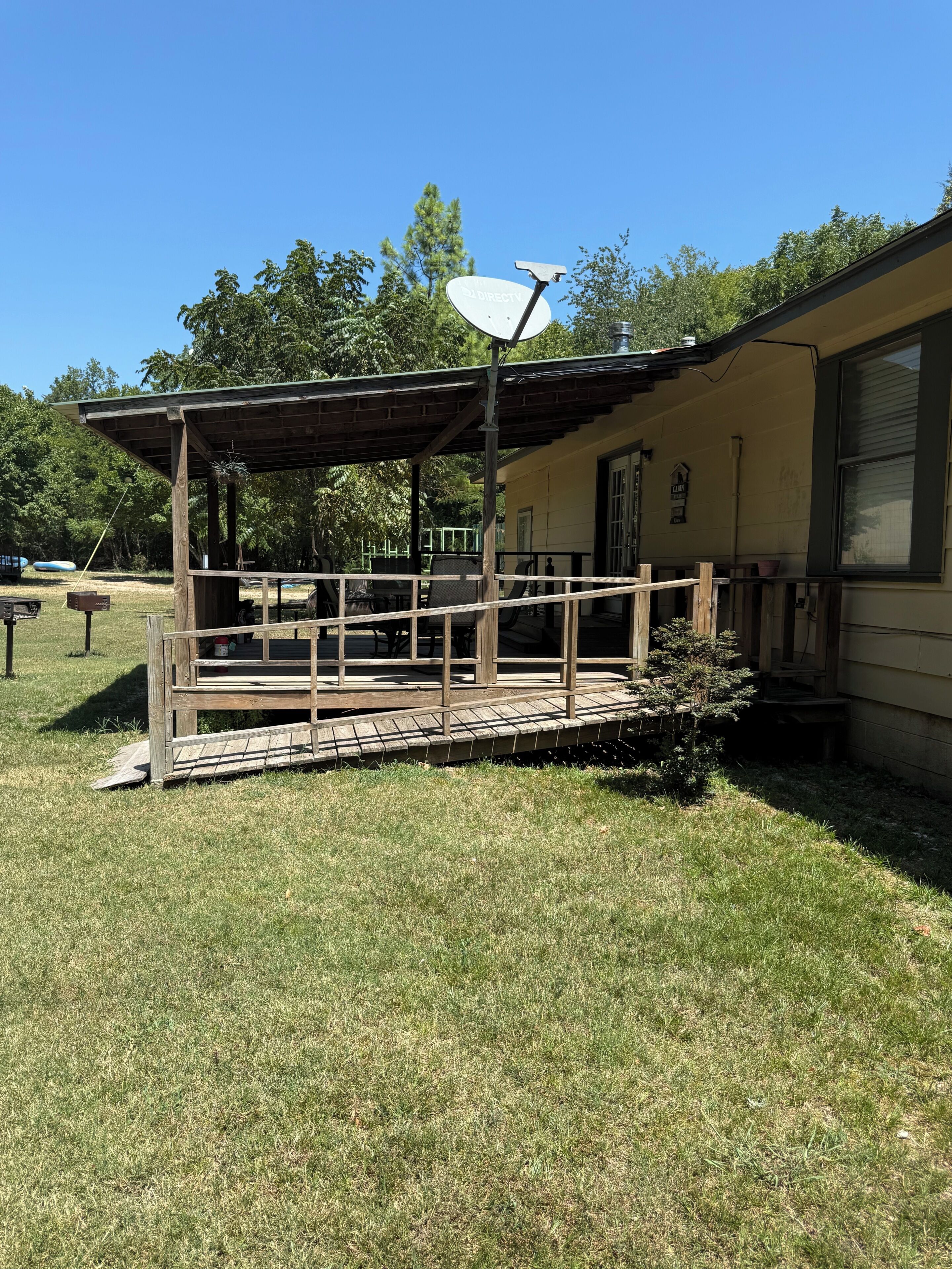 A covered outdoor seating area with a satellite dish, a wooden deck, and a house in the background.