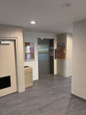 A hallway with a door, an elevator, and a trash bin. - Bright renovated studio steps from Bonita Beach & balcony gulf breezes all day (Bonita Springs)
