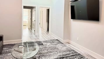 A hallway with a glass table, a black and white patterned rug, and a mounted television on the wall.