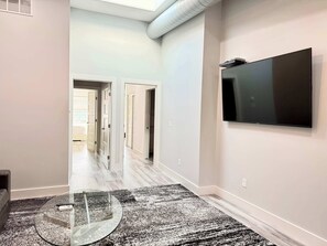 Un couloir avec une table en verre, un tapis à motifs noir et blanc et un téléviseur fixé au mur.