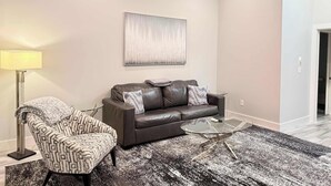 Ein modernes Wohnzimmer mit Ledersofa, gemustertem Sessel und Glastisch.