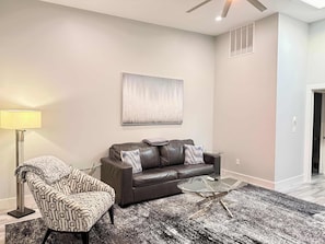 A modern living room with a leather sofa, patterned armchair, and a glass coffee table. - Downtown Apt w/ Balcony & Free Parking (Geneva)