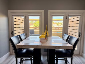 A dining area with a marble table, black upholstered chairs, and a view through wooden slats. - Downtown Apt w/ Balcony & Free Parking (Geneva)
