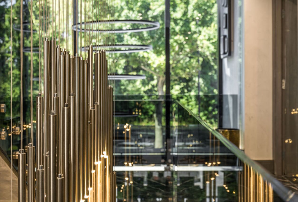 Een modern interieur met verticale verlichtingsarmaturen en een glazen balustrade met uitzicht op een groen buitengebied.